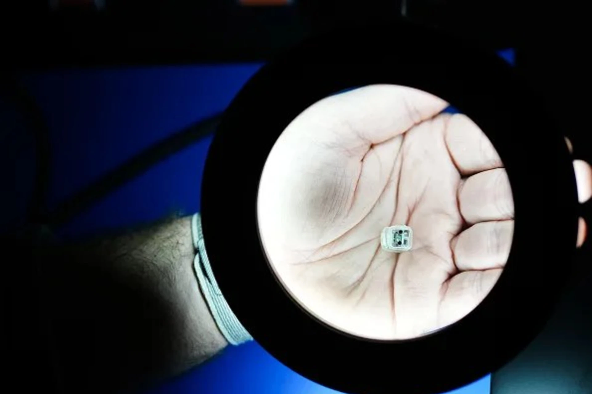 <p>Motif CEO and founder Jacob Robinson holds a prototype of a pea-size device that would be implanted into the skull under a microscope in January 2024 in Houston. Rice University students will continue to develop the device, with support from the Rice Biotech Launch Pad.</p>
