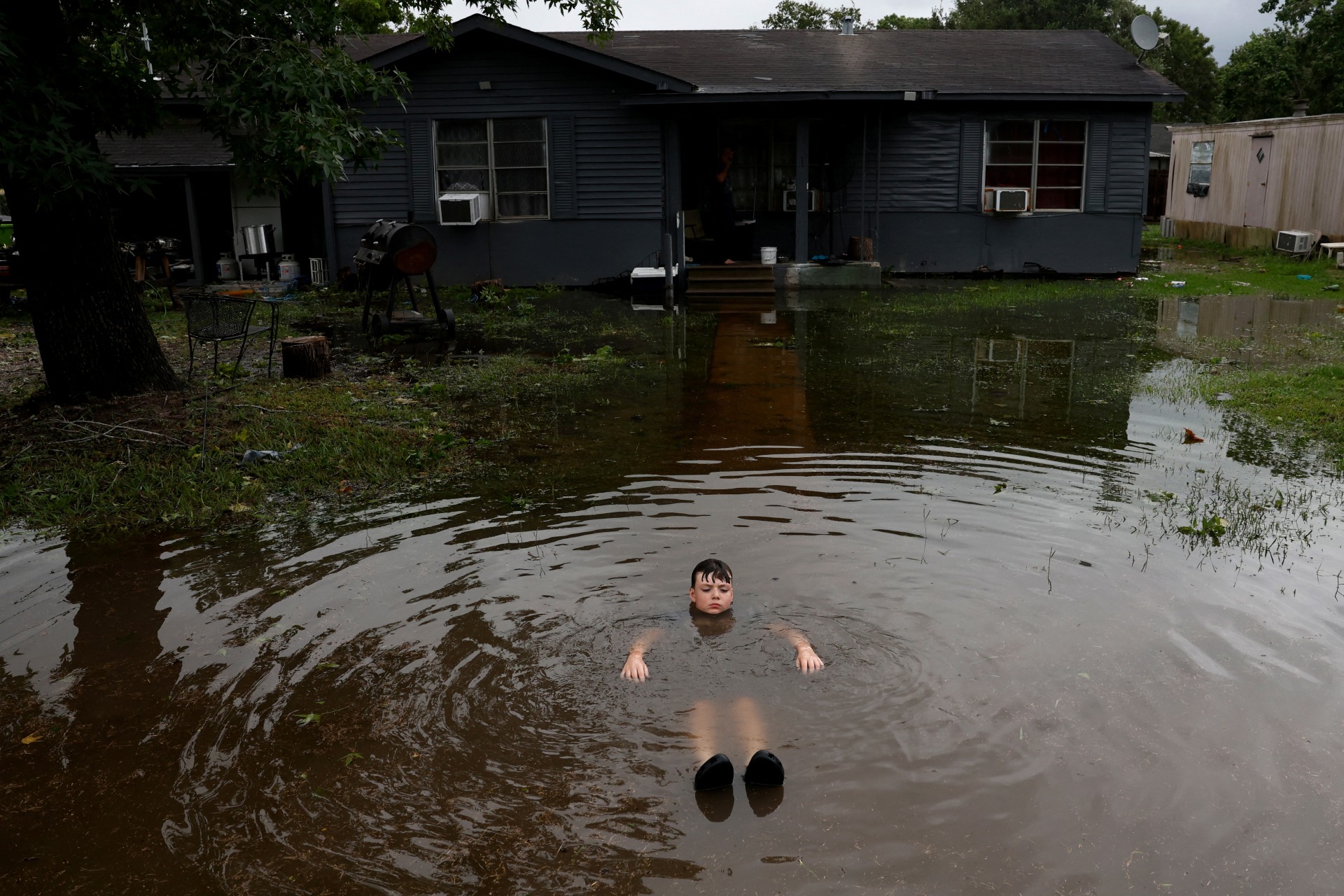 Boy immerses himself in flood waters outside a home in the aftermath of Hurricane Beryl