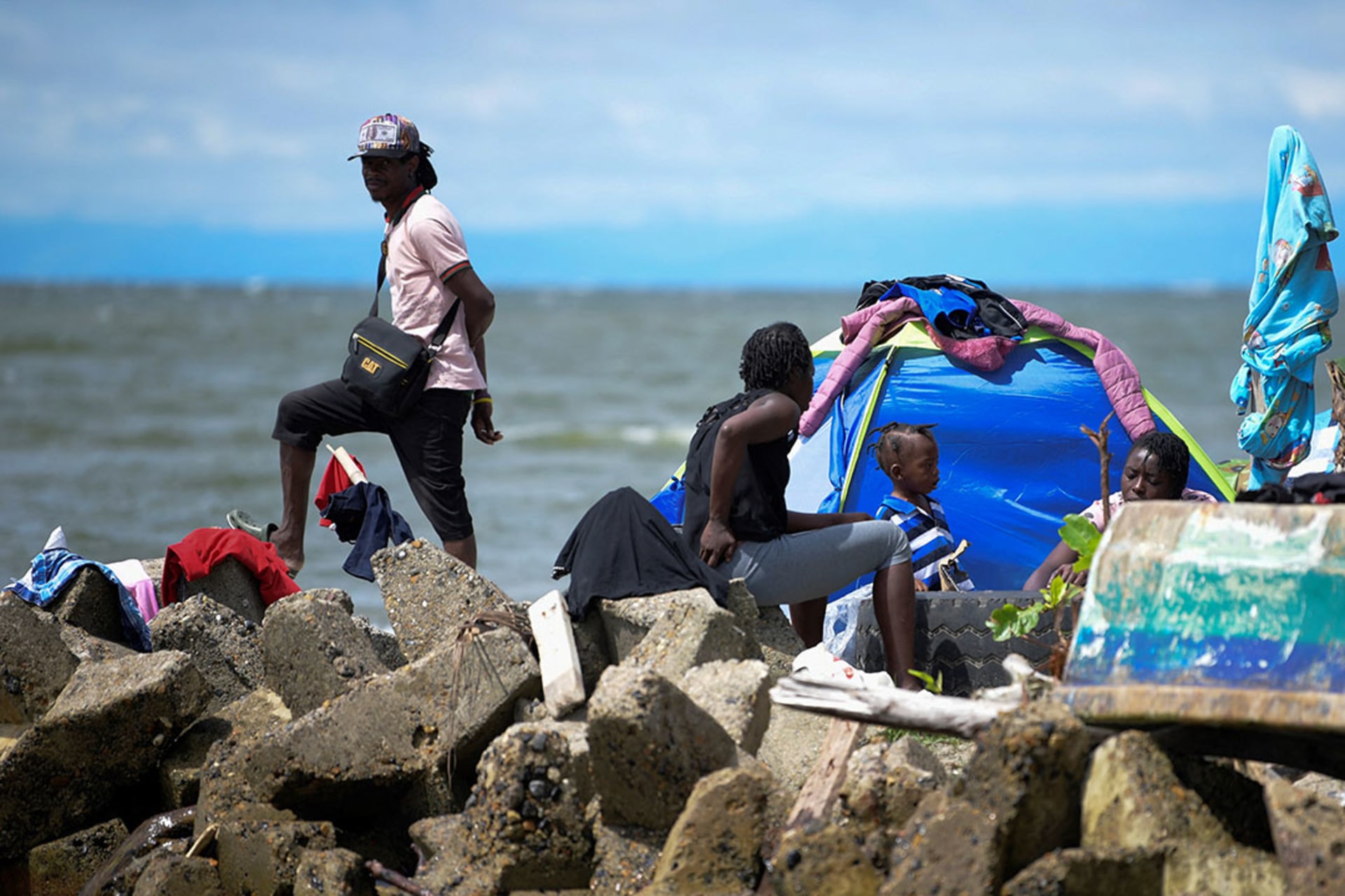 A stranded migrant from Haiti, standing on rocks, waits with other migrants to travel to the border with Panama in Necocli, Colombia.