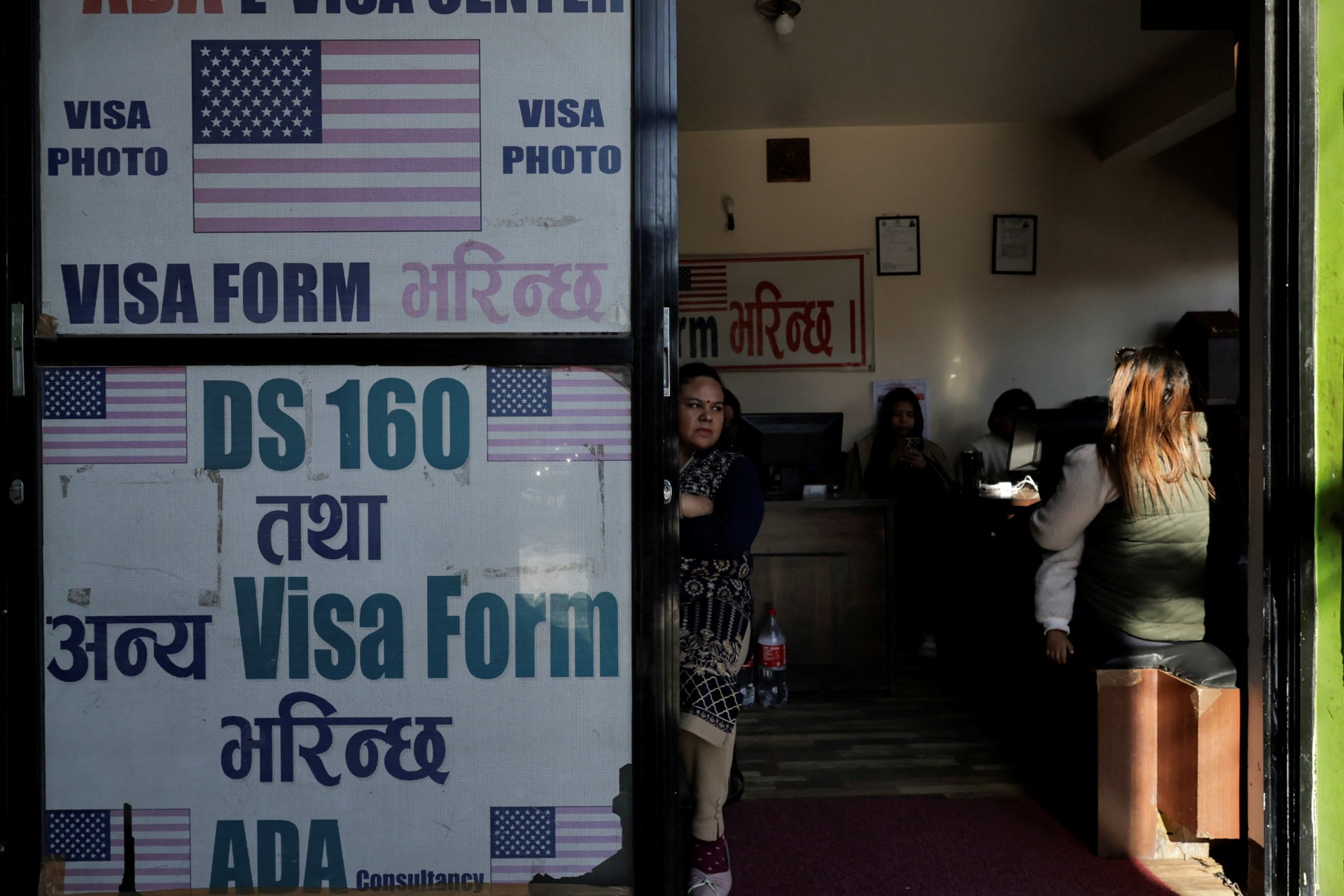 A woman holding a child sits at a visa consultancy, in Kathmandu