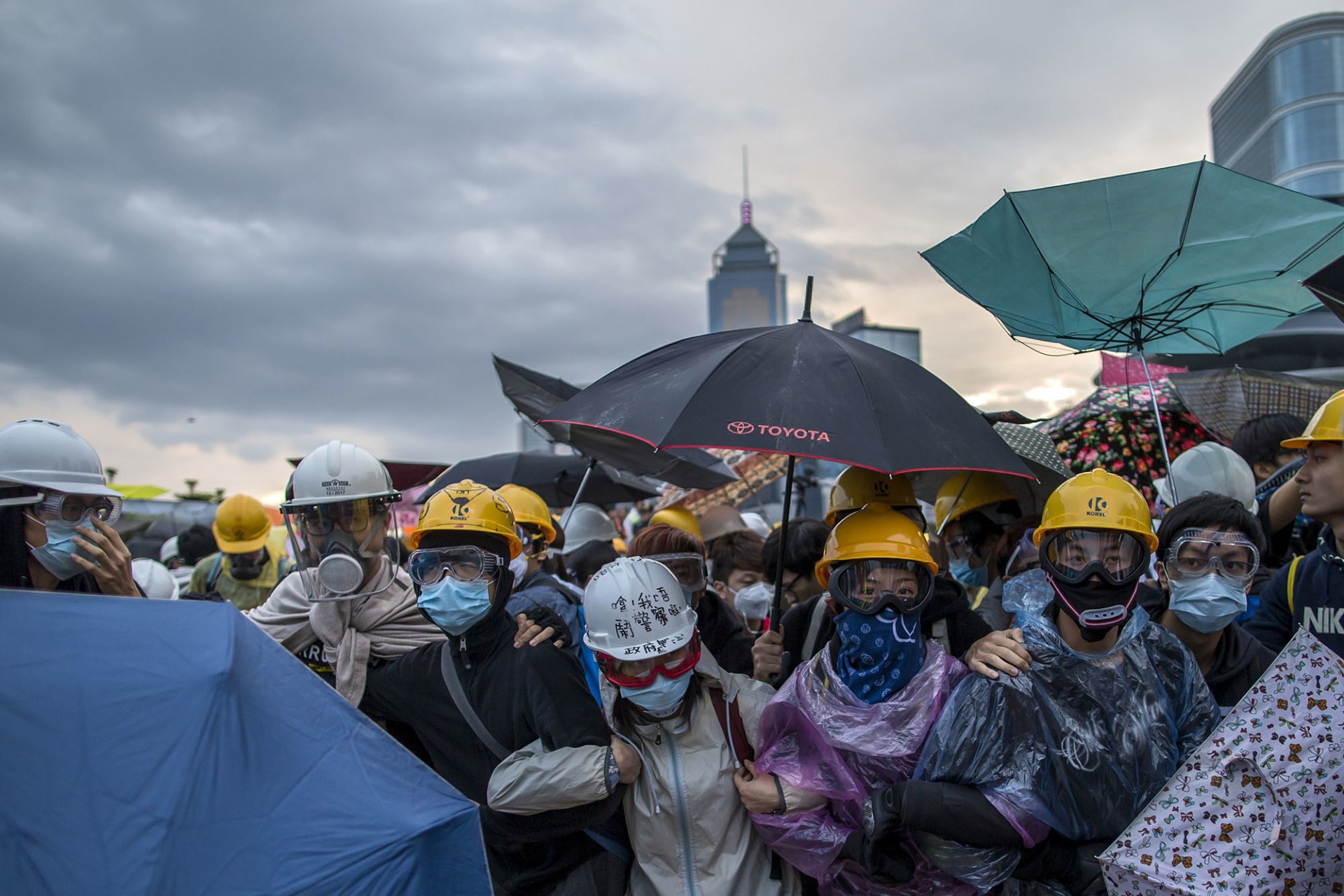 Image of protesters in masks and holding umbrellas.