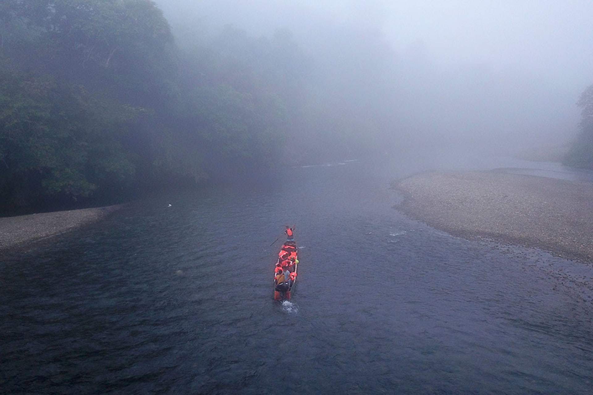 View of small boat, navigating through fog on a river, transporting migrants.