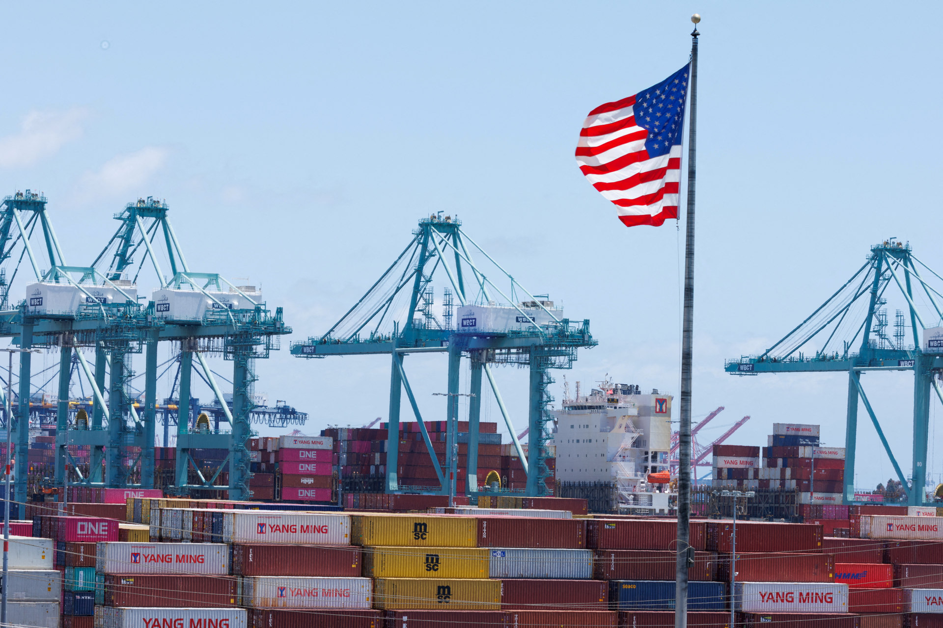 An American flag flutters over a ship and shipping containers at the Port of Los Angeles, in San Pedro California, U.S., May 13, 2025. REUTERS/Mike Blake/File Photo