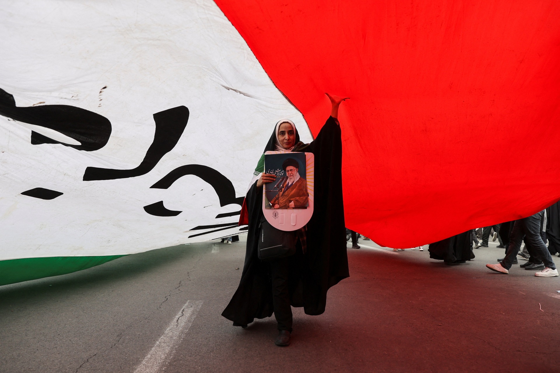 An Iranian woman holding a poster depicting Iran's Supreme Leader Ayatollah Ali Khamenei walks under a large flag during the forty-seventh anniversary of the Islamic Revolution in Tehran, Iran on February 11, 2026. Majid Asgaripour/West Asia News Agency via Reuters