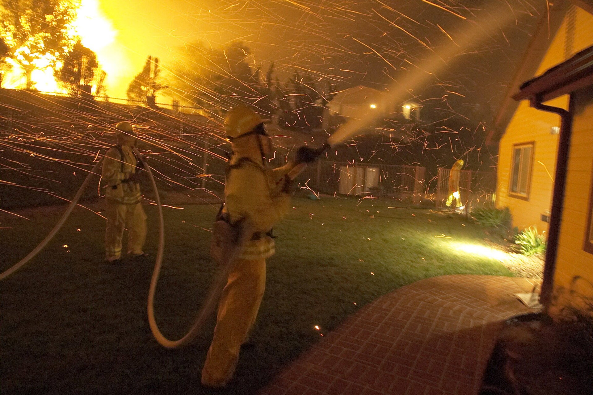 FIREFIGHTERS HOSE DOWN HOME TO PROTECT IT FROM BURNING EMBERS.