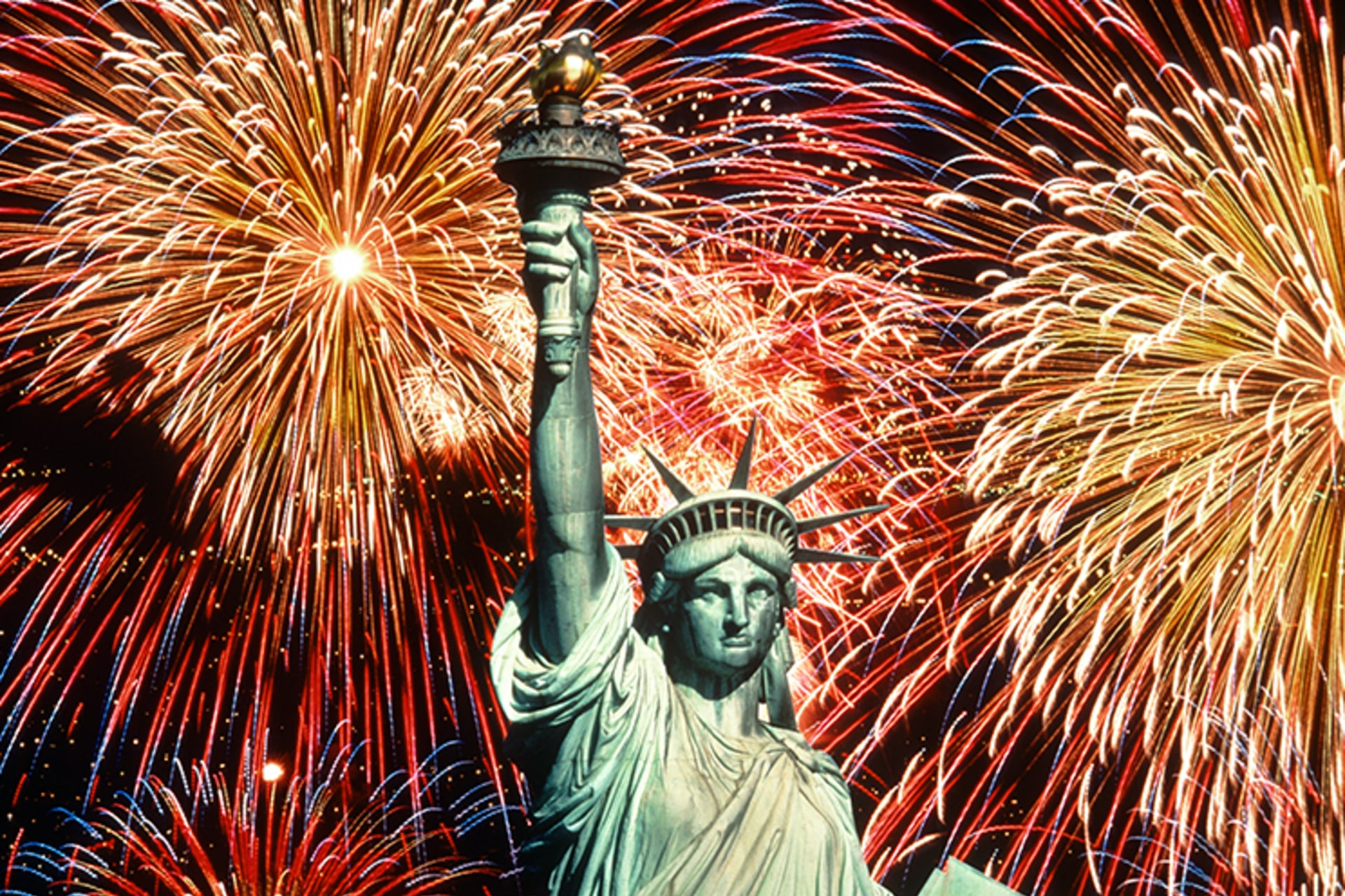 The statue of liberty backlit by fireworks in the night sky.