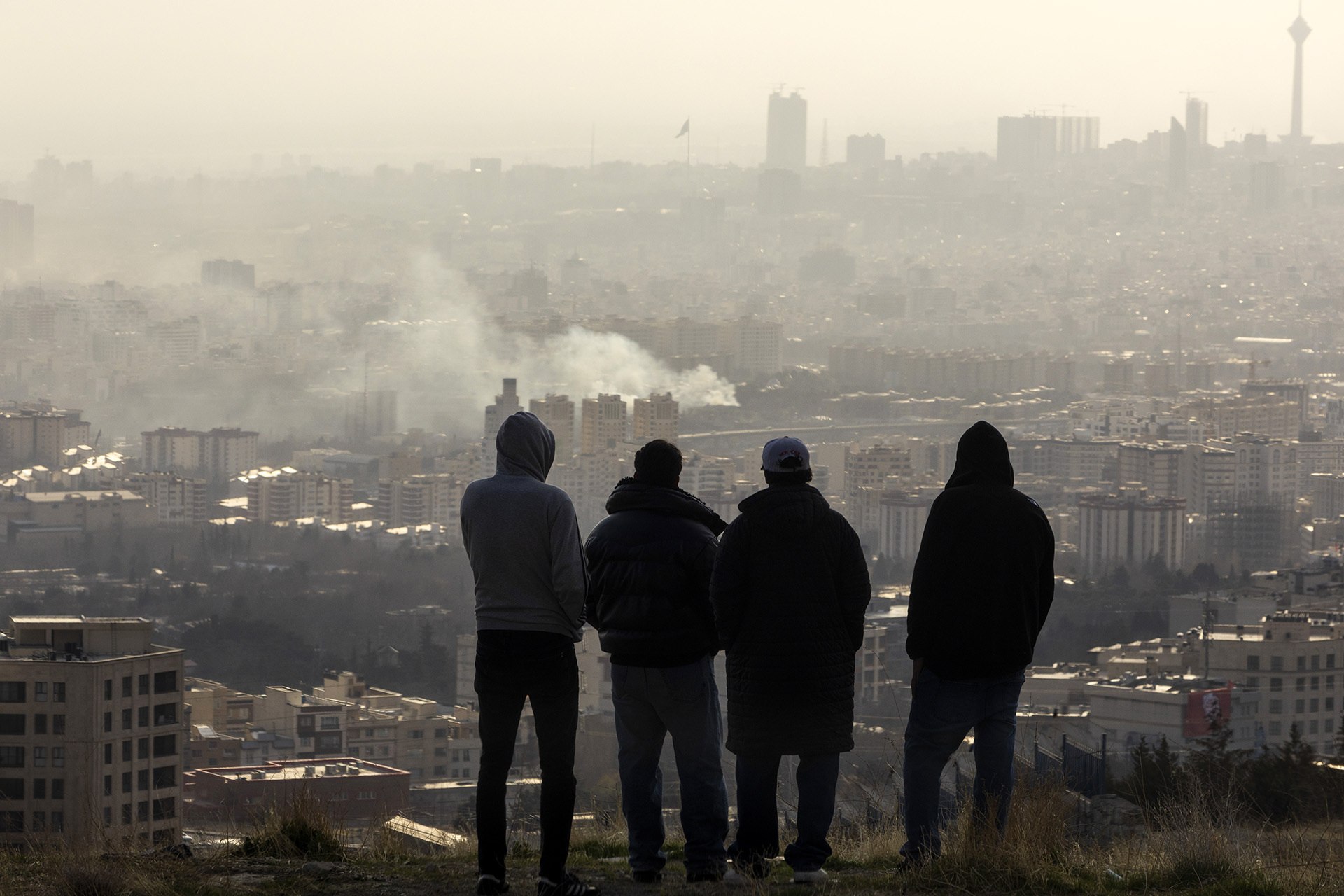 <p>Men watch from a hillside as a plume of smoke rises after an explosion on March 2, 2026 in Tehran, Iran.</p>
