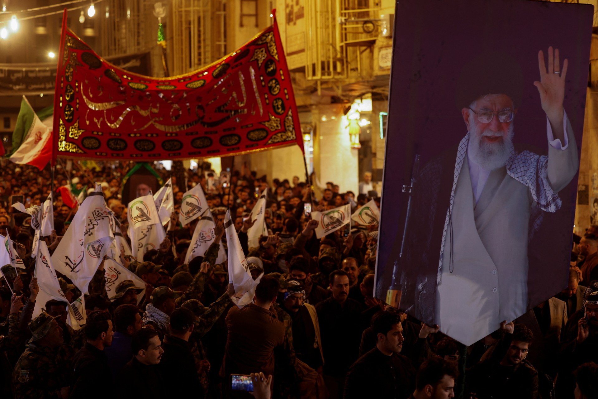Mourners hoist banners and a large photograph of Supreme Leader Ali Khamenei at a symbolic funeral procession in Najaf, Iraq.