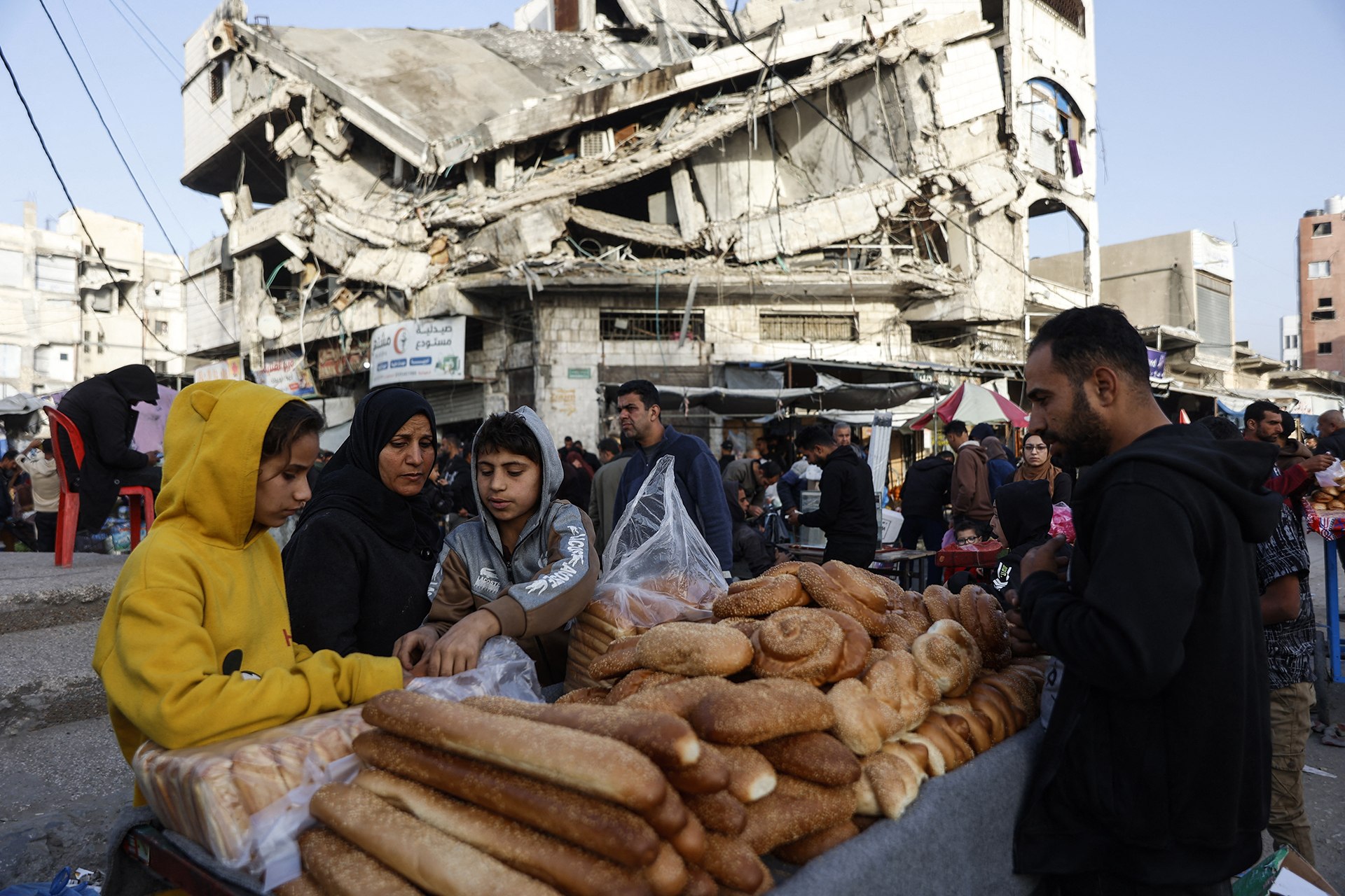 Palestinians sell bread on a street beneath a destroyed building in Gaza City's Zawiya market on February 18, 2026, on the first days of the holy fasting month of Ramadan.
