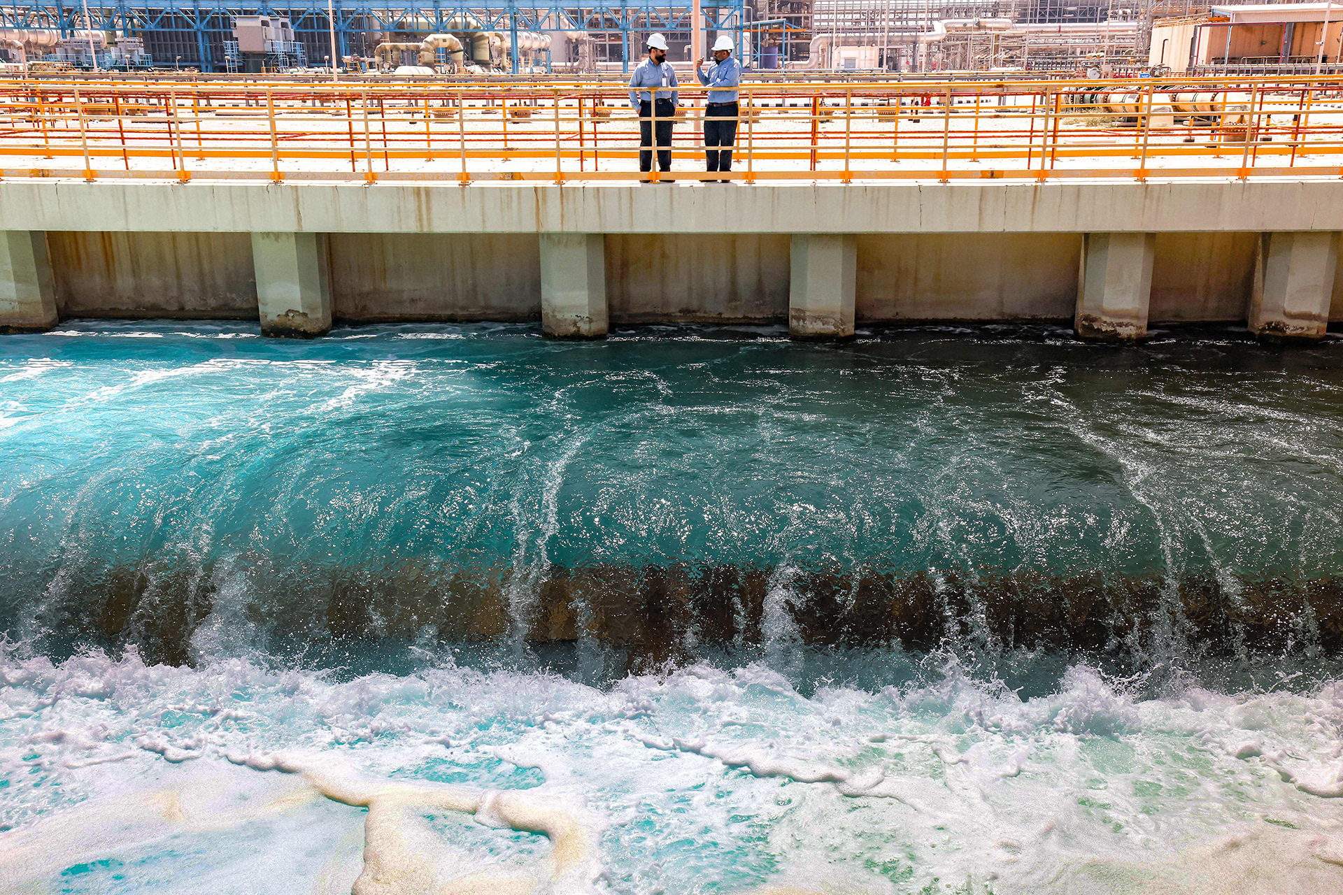 A manager at the Ras al-Khair water desalination plant speaks with an employee at the facility in Ras al-Khair along the Gulf coast in eastern Saudi Arabia. Water flows underneath them while they stand on a concrete platform.