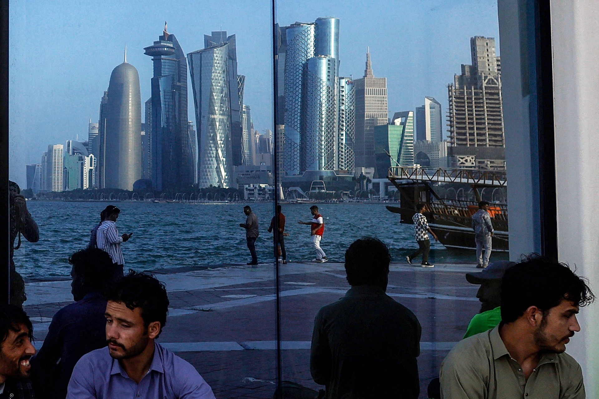 People sit with the reflection of the Doha skyline along the Doha Corniche, on the second day of Eid al-Fitr celebrations marking the end of the Muslim holy month of Ramadan, in Doha on March 21, 2026.