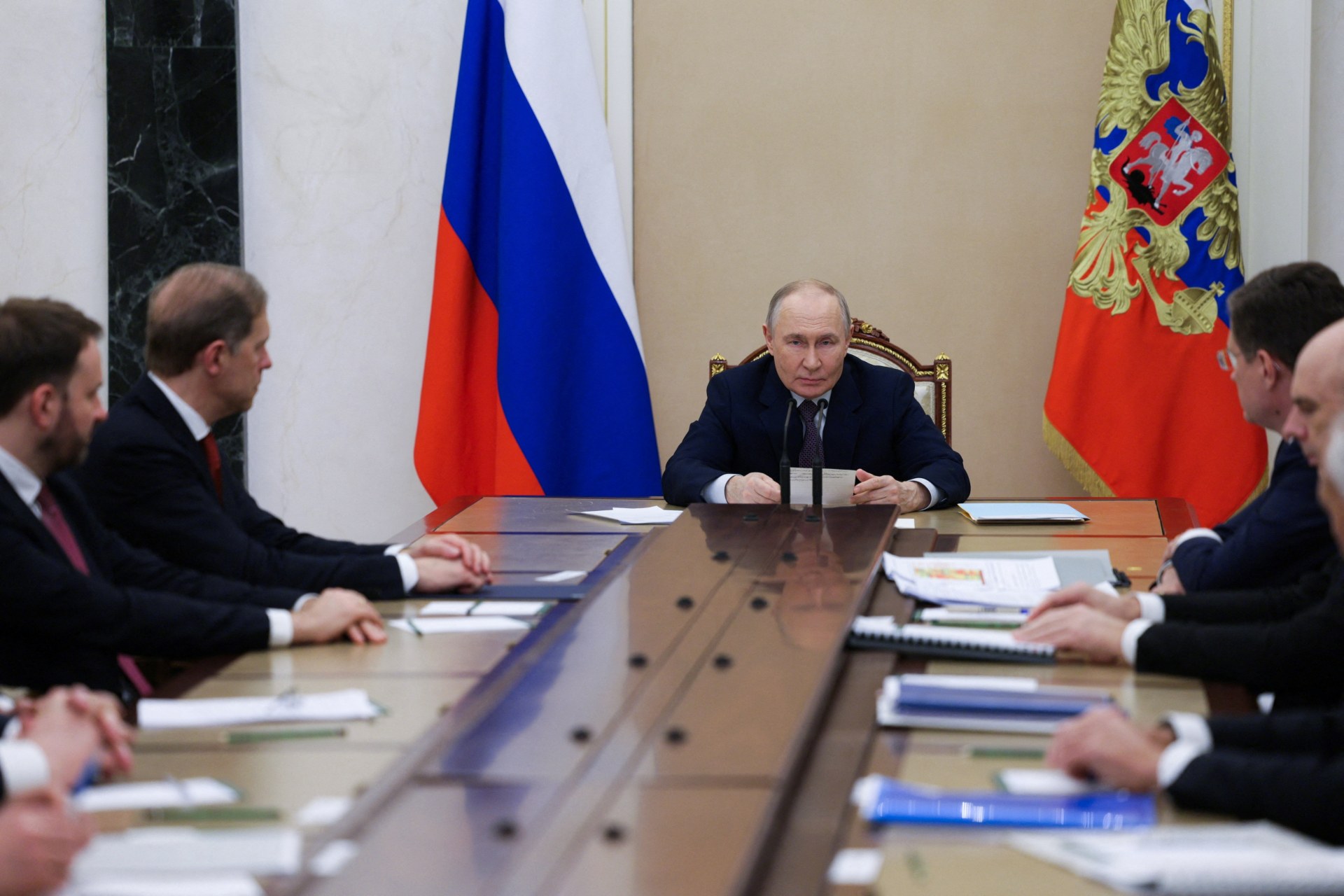 Vladimir Putin sits at the end of a long conference table surrounded by advisors.