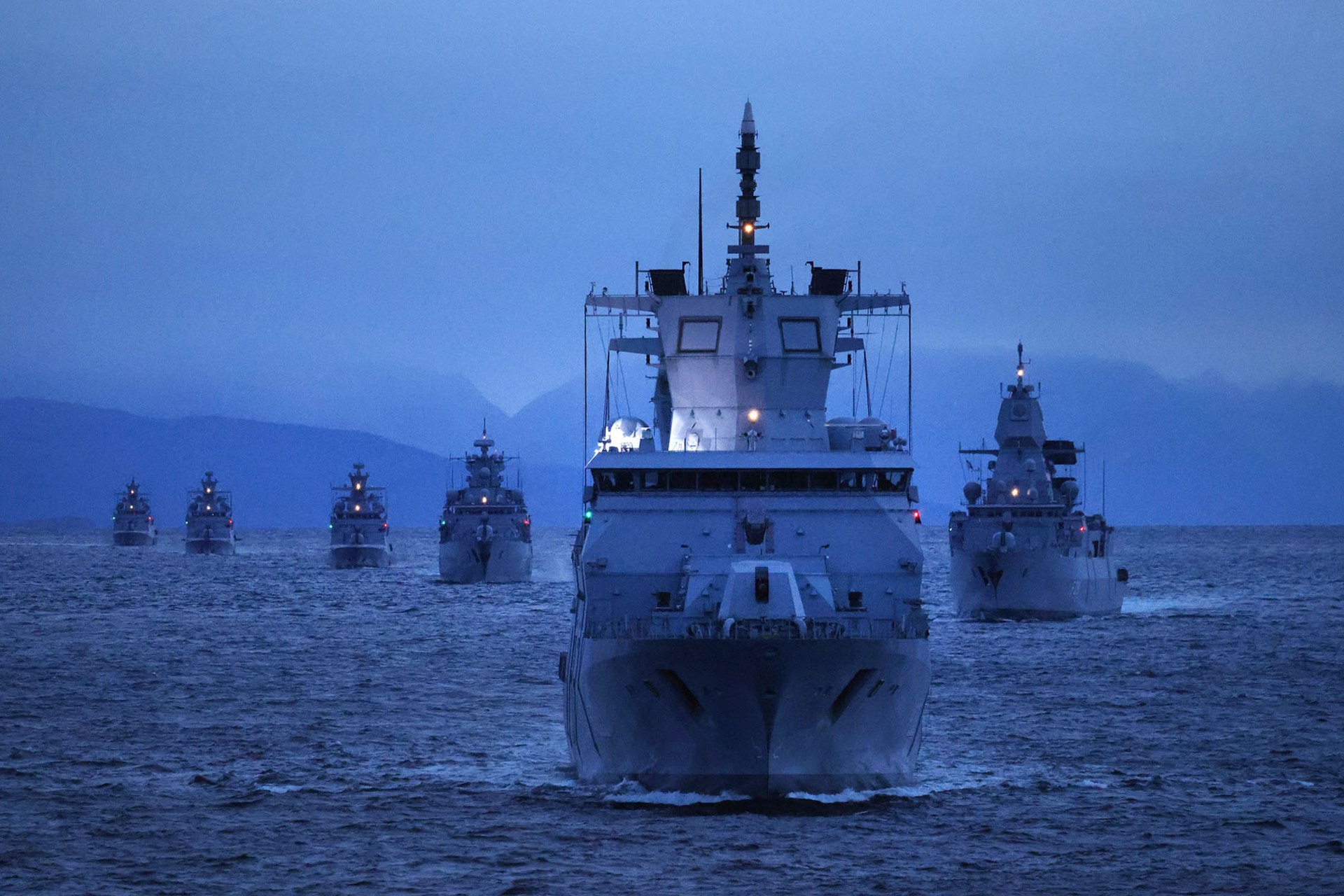 Six battleships sail on open water at twilight