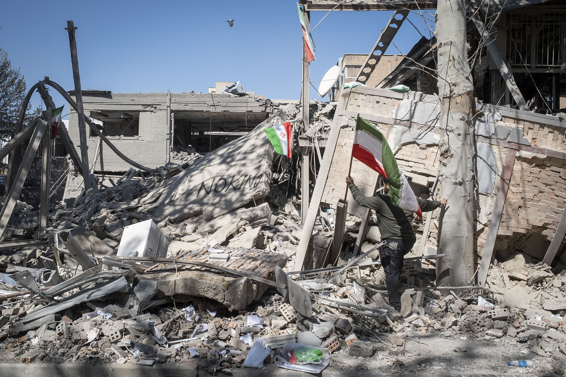 An unidentified man places a national flag on the ruins of the Sharif University of Technology's data center, which was struck on April 6 during ongoing military operations in Tehran, Iran, on April 7, 2026.