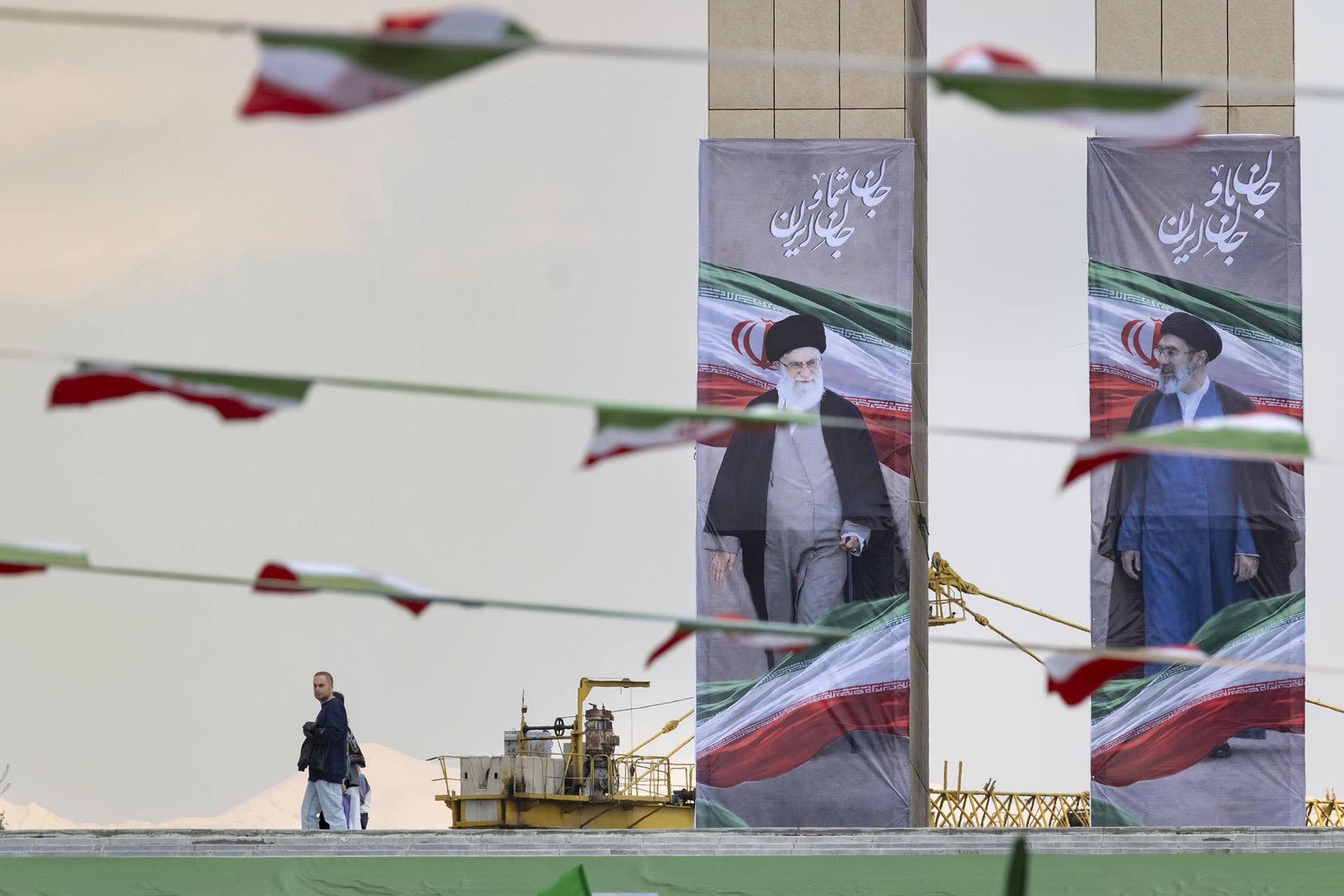 An Iranian man walks past the portraits of late Supreme Leader Ayatollah Ali Khamenei and the new Supreme Leader Ayatollah Mojtaba Khamenei during a flag ceremony marking Iran's Islamic Republic National Day in the Abbasabad Cultural and Tourist Area in central Tehran, on April 1, 2026.