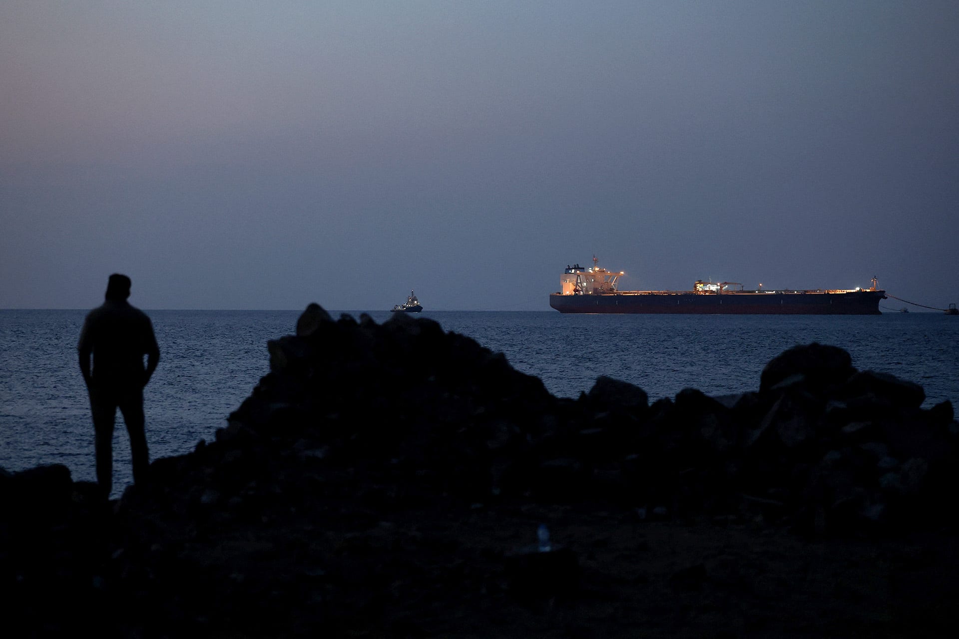 Person watches an oil tanker from shore at night.