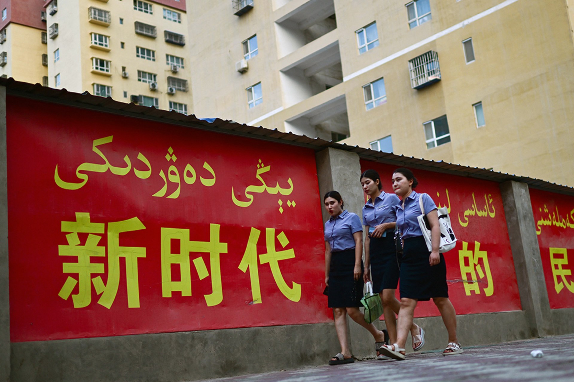 Women walk past a propaganda slogan in both Chinese and Uyghur languages, in Yarkant, Xinjiang.