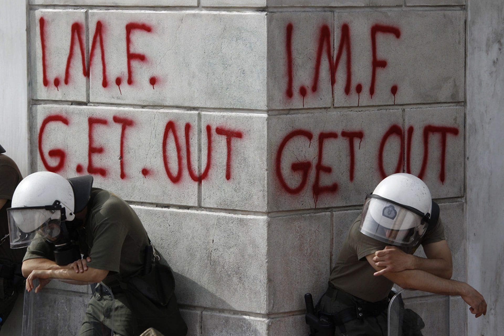 Greek riot policemen rest in front of graffiti written on the wall of a bank in Athens during violent demonstrations over austerity measures demanded by the May 2, 2010, EU-IMF bailout. 
