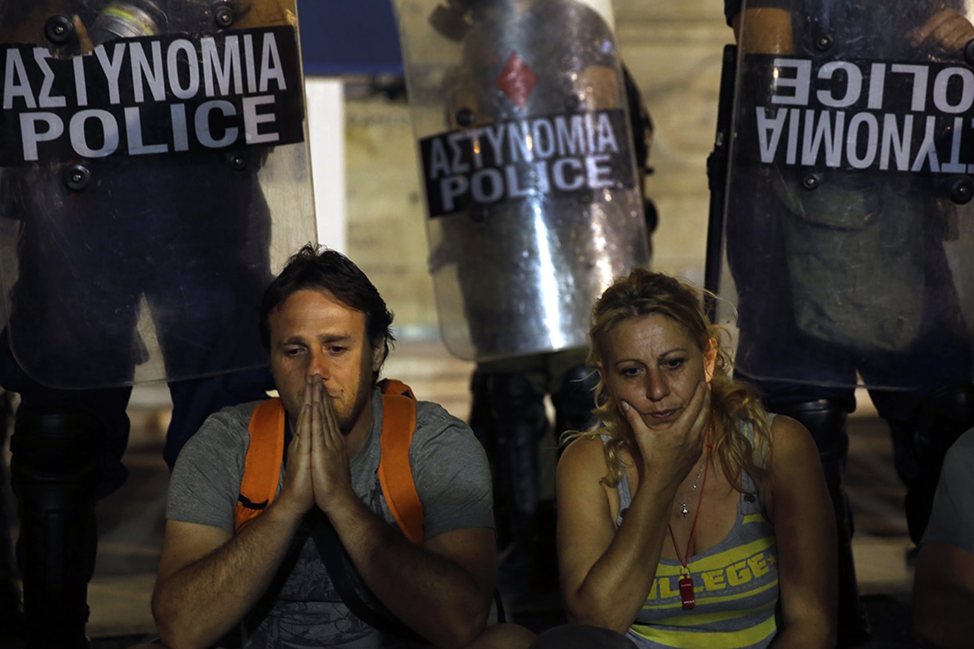 Municipal public school guard Yiorgos Avramidis and a colleague, who lost their jobs due to government budget cuts, sit in front of a police line guarding the Greek parliament on July 17, 2013. 
