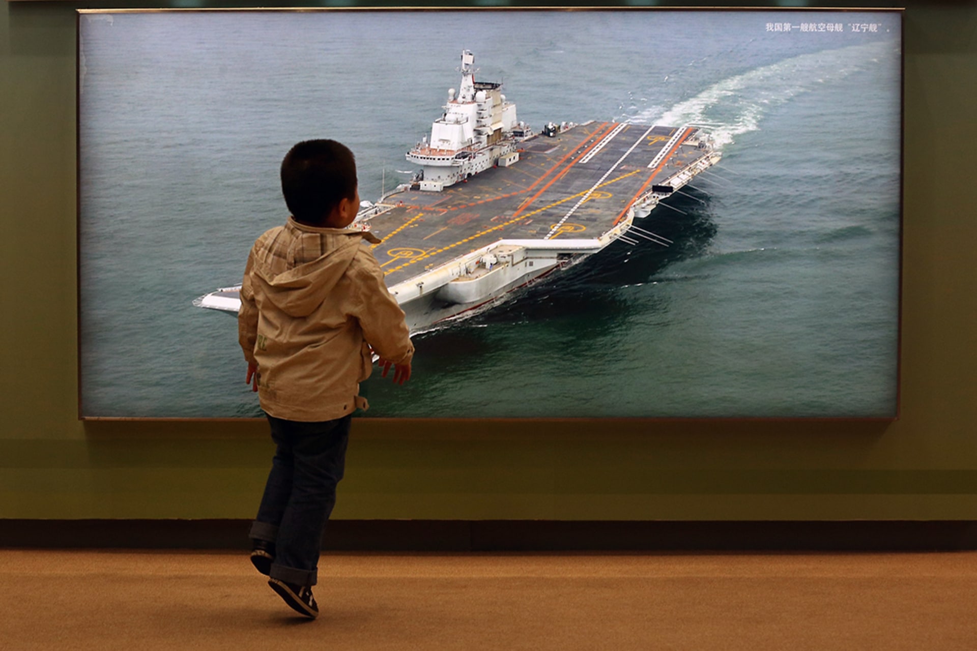 A Chinese boy passes a photo of China’s first aircraft carrier at an exhibition. Feng Li/Getty Images