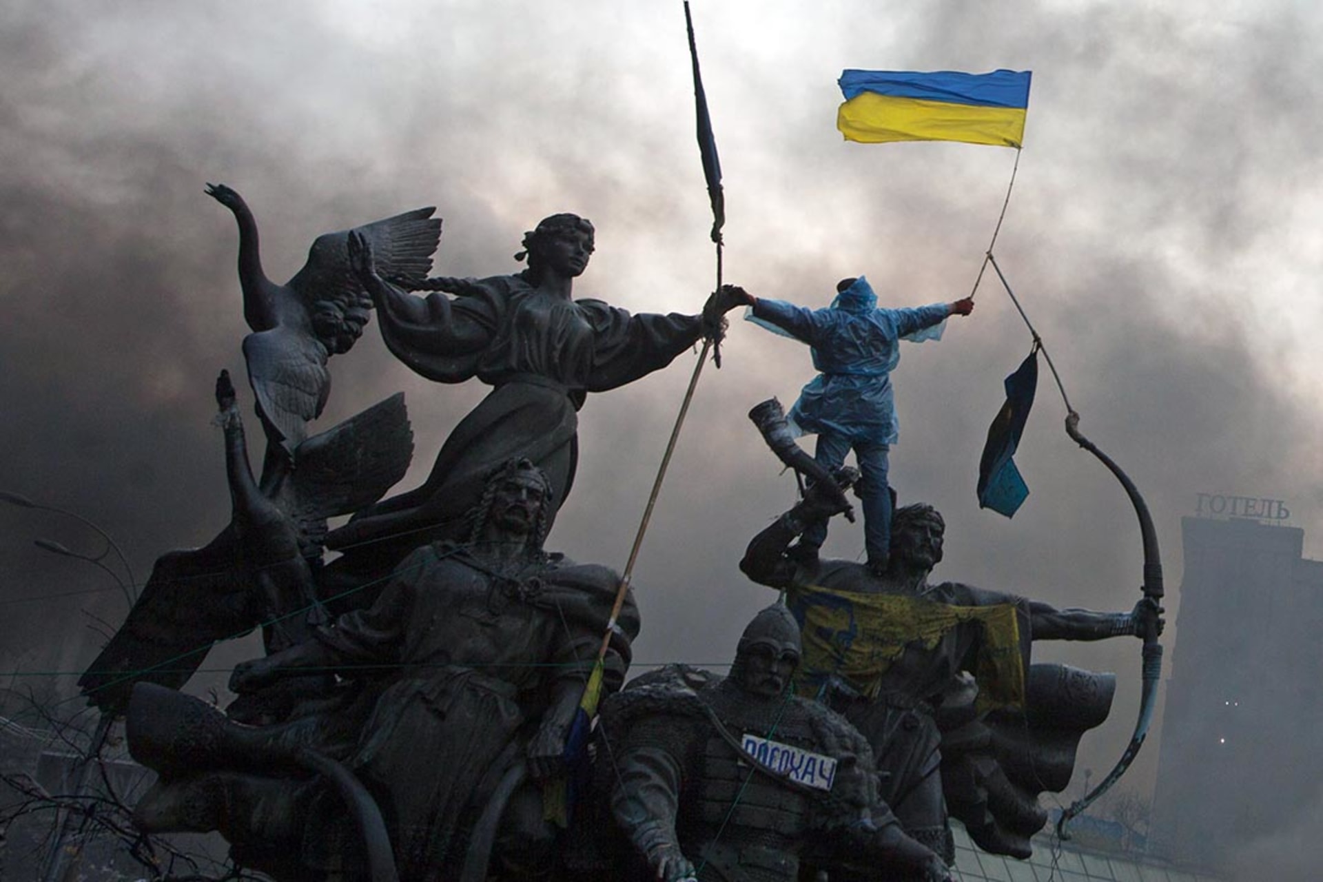 An anti-government protester waves the national flag from the top of a statue during clashes with riot police in Independence Square in Kyiv.