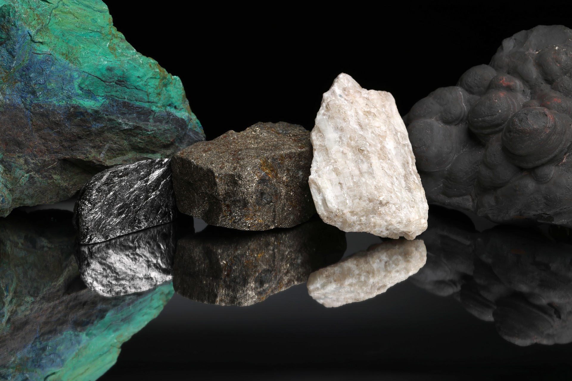 Critical mineral ores, including copper, graphite, nickel, lithium, and manganese, against a black background and reflected on a mirrored table.