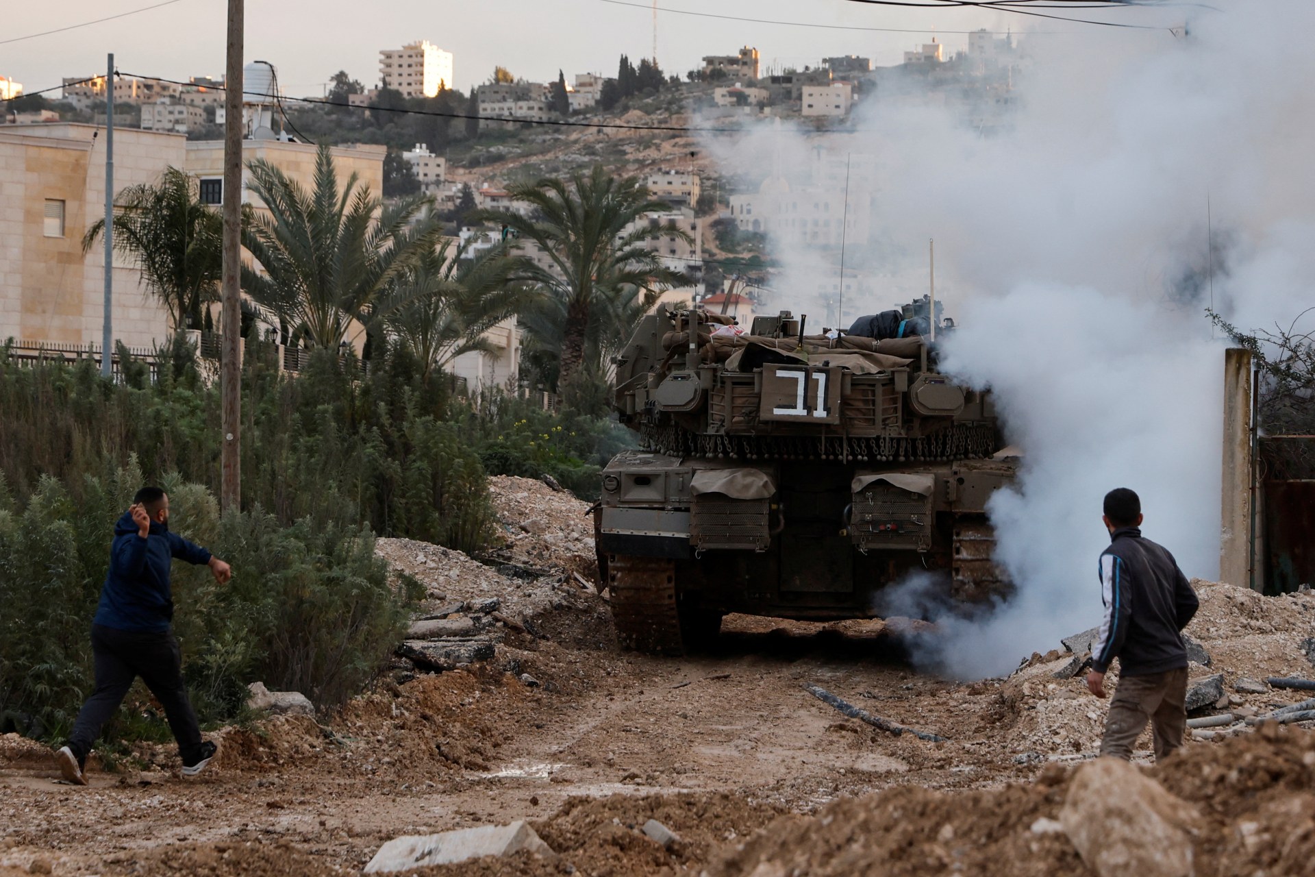A man prepares to throw an object as an Israeli tank operates during an Israeli operation in Jenin, in the Israeli-occupied West Bank